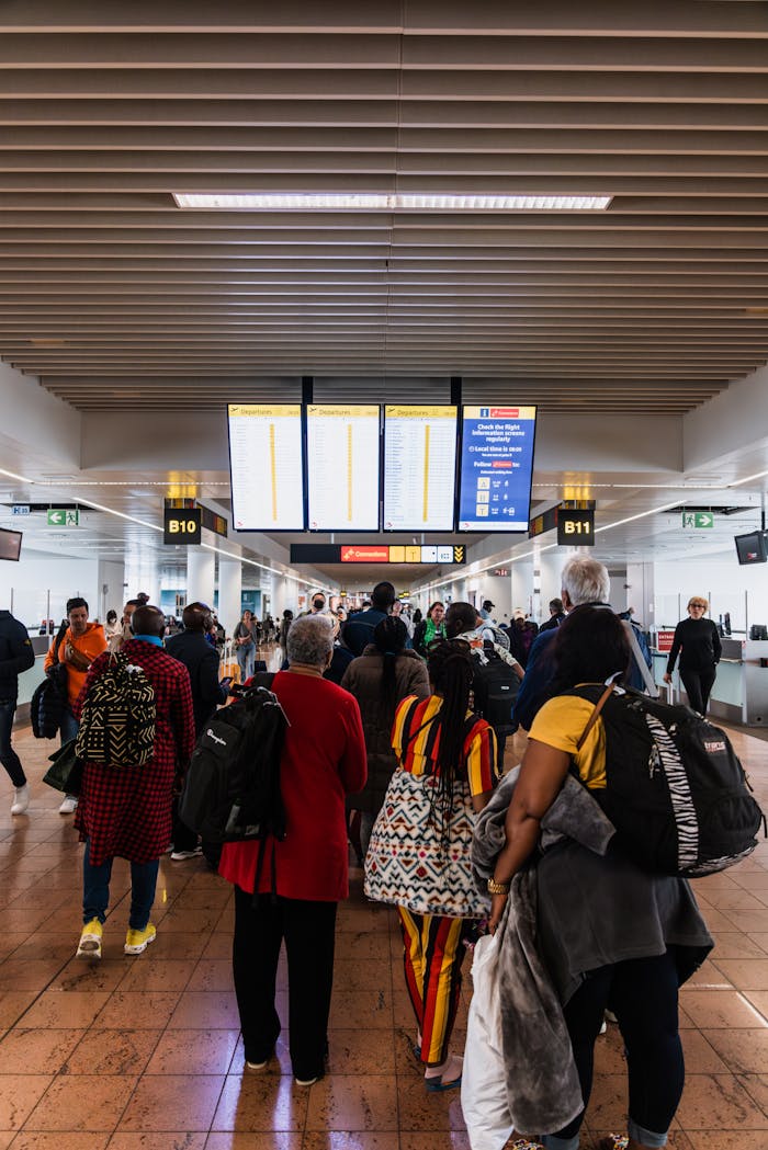 Travelers lining up in a busy airport terminal with baggage under flight information screens.
