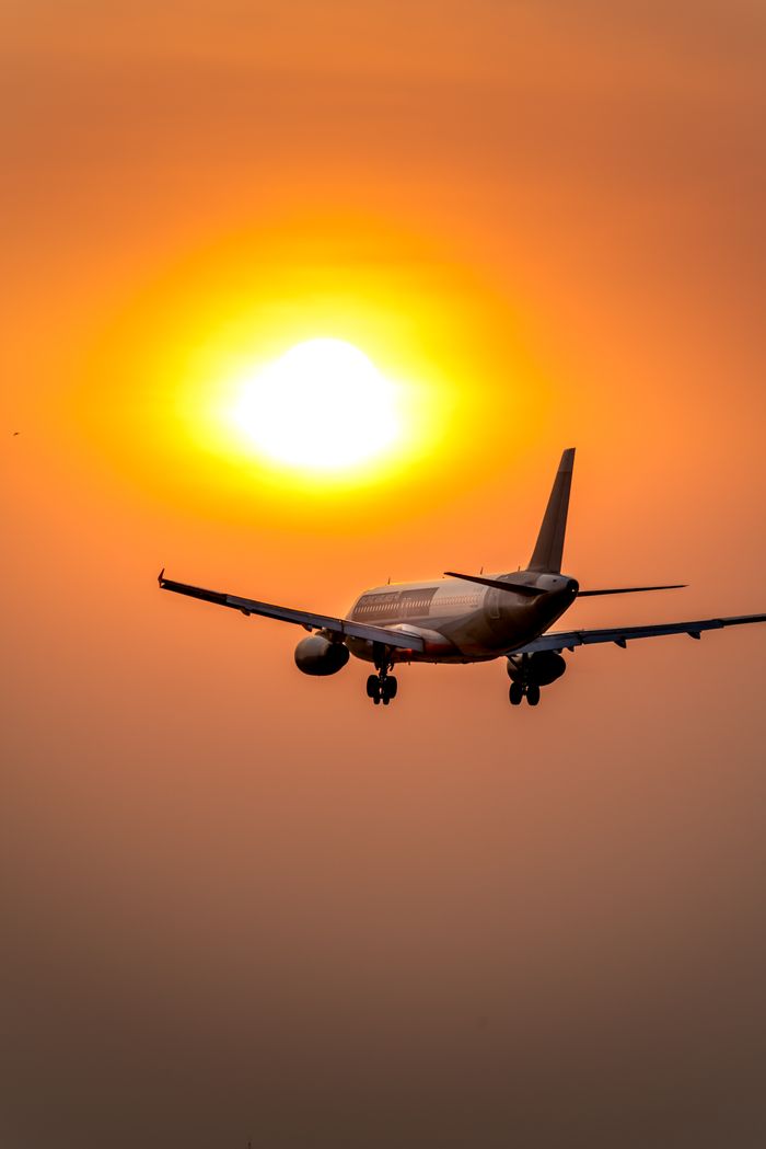 Airplane soaring towards a golden sunset sky, creating a dramatic silhouette.